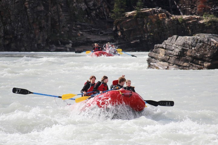 Group rafting on a river in red inflatable rafts, navigating through rocky rapids.