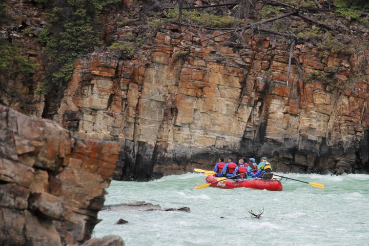 Group of people white-water rafting near rocky cliff face.