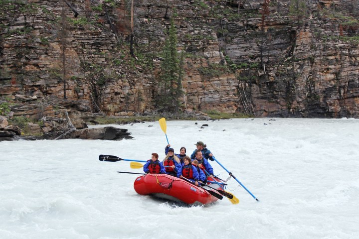 Group of people whitewater rafting on a river near rocky cliffs.