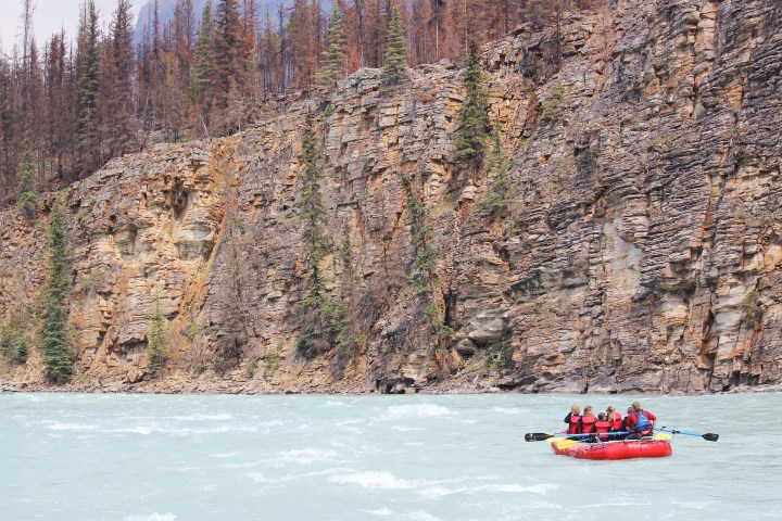 Group rafting on a wide river with rocky cliffs in the background.