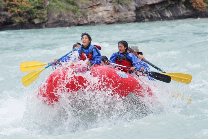 People in a red raft paddling through rapids with smiles and splashes of water.