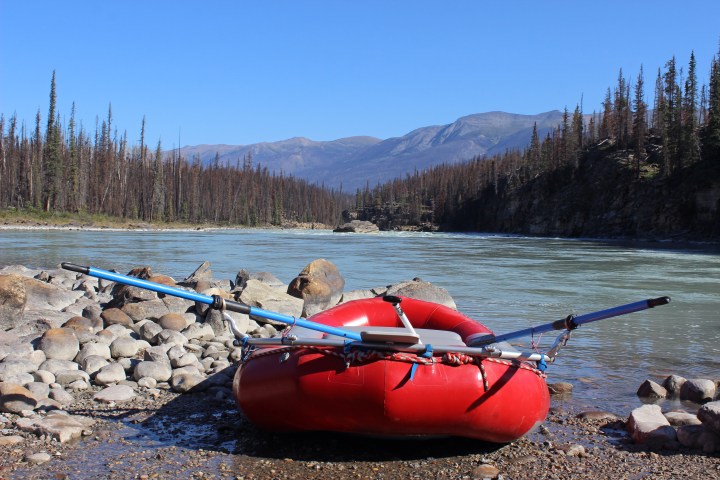 Red inflatable raft on rocky riverbank with forested mountains in background.