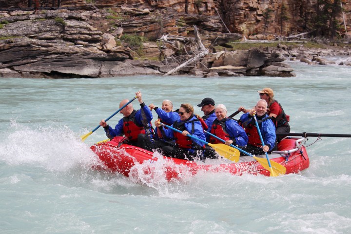 Group of people whitewater rafting on a river in a red inflatable raft.