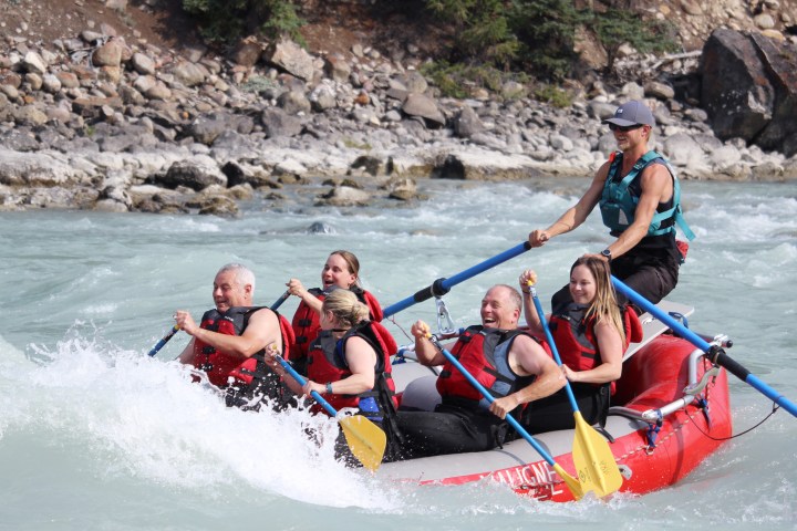 Group of people in red raft paddling through rapids on a river.