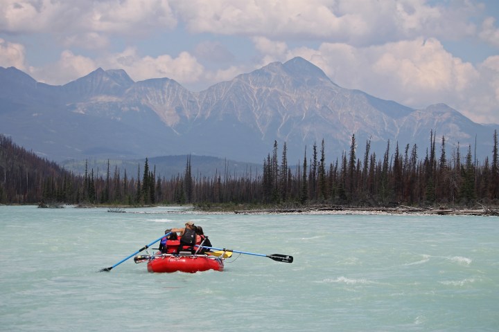 People rafting on a river with mountains and trees in the background.