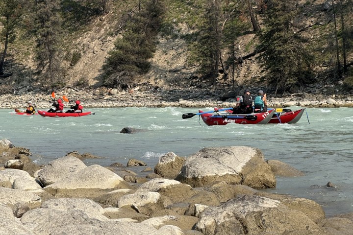 People rafting and canoeing on a rocky river with forested banks.