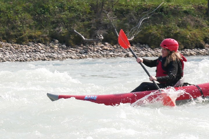 Person in red kayak paddling through whitewater rapids, wearing a red helmet and life jacket.