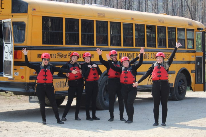 Six people in red helmets and life vests pose excitedly in front of a yellow school bus.