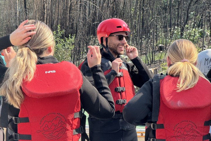 People in red life jackets and helmets preparing for outdoor activity in wooded area.