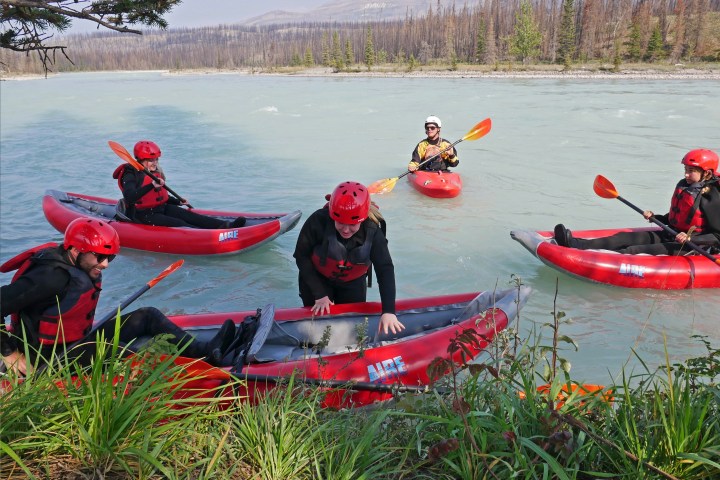 Five people in red kayaks on a river, wearing helmets and life vests.