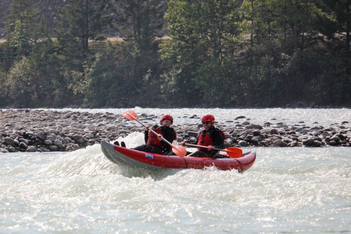 Two people in helmets and life jackets kayaking on a river with rapids.