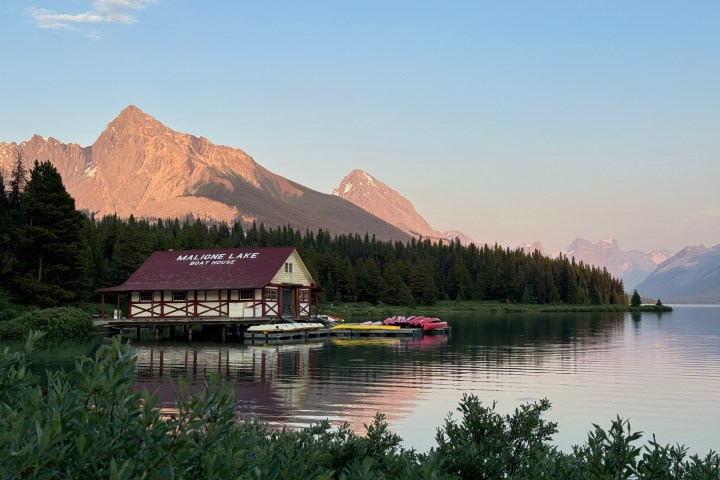 Scenic lake view with boathouse, mountains, and forest at sunset.