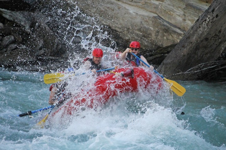 Two people in helmets rafting on a turbulent river with paddles.