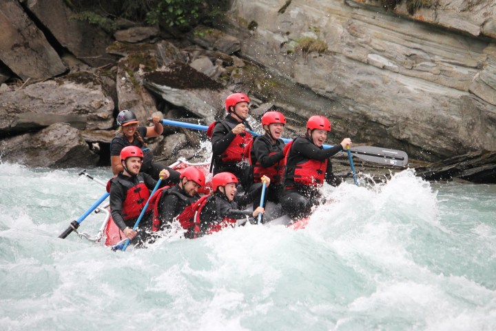 Group of people white-water rafting with helmets and paddles in a rapid river.