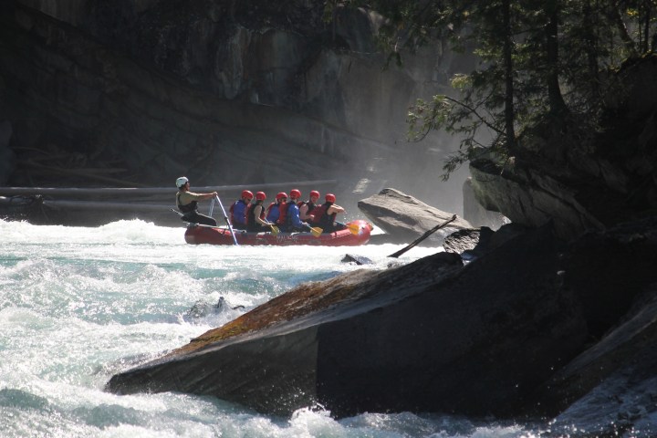 Rafters navigating a rocky river in a red inflatable raft under partial sunlight.