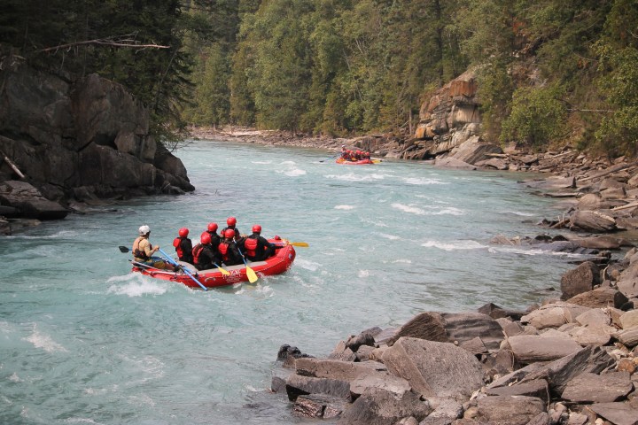 People rafting on a clear river with rocky banks and forested surroundings.