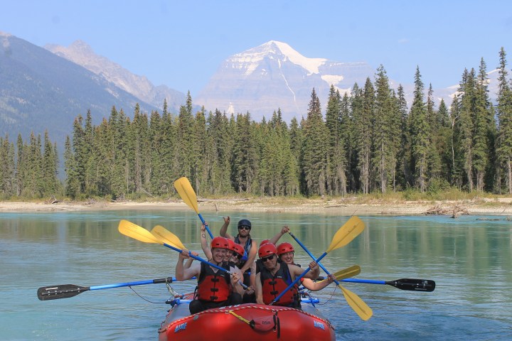 Group rafting on a river with snowy mountain in the background.