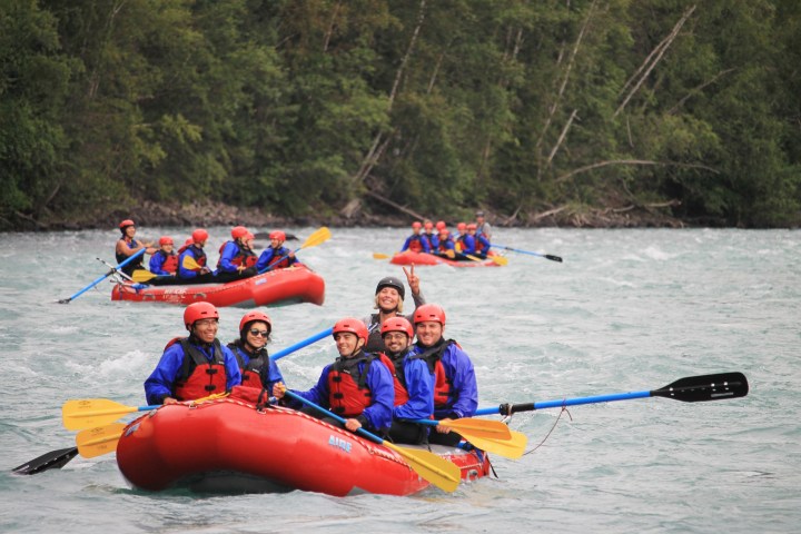Group of people whitewater rafting in inflatable red boats on a river.