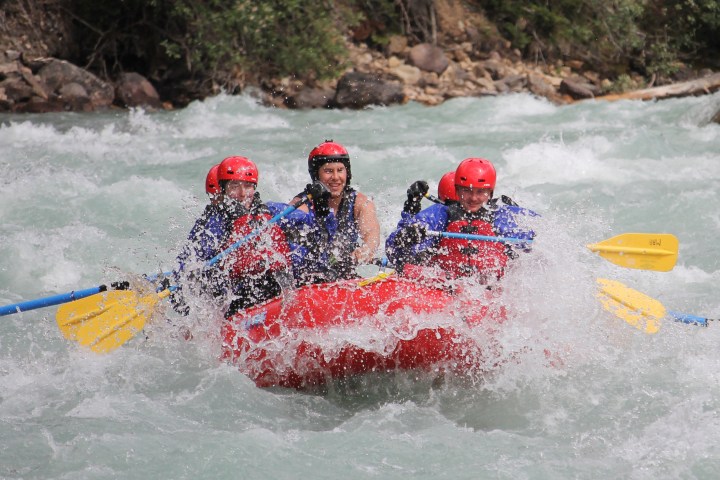 Group whitewater rafting in red raft with yellow paddles on a turbulent river.