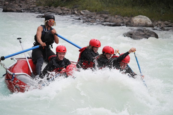 Group of people whitewater rafting with helmets and life jackets.