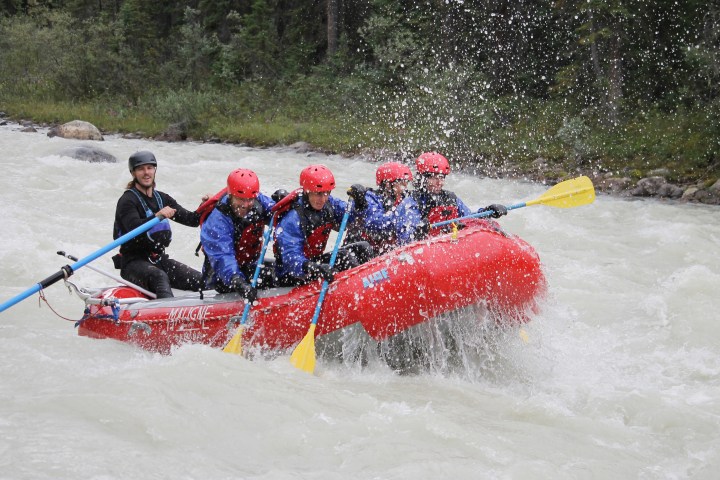 Group of people white-water rafting in a red inflatable raft on a river.