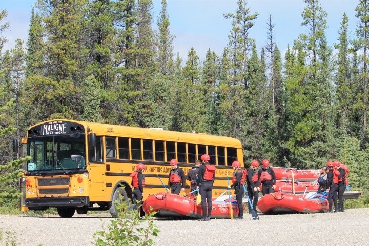 Group in helmets by yellow bus and red rafts in a forest setting.