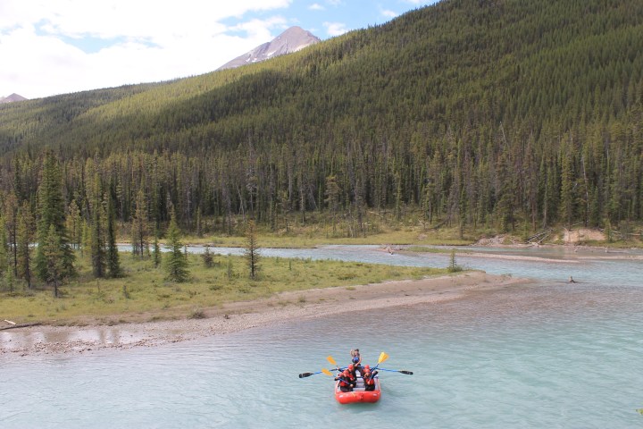 Group rafting on a turquoise river in front of a forest and mountain landscape.